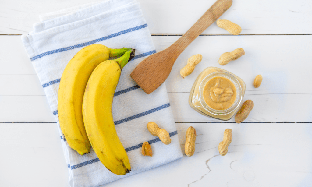 bananas and wooden spoon on a towel with a small jar of peanut butter.